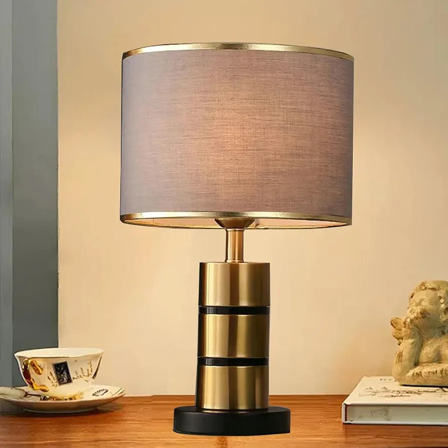 Brass gold table lamp with grey fabric drum shade and black base on wooden surface