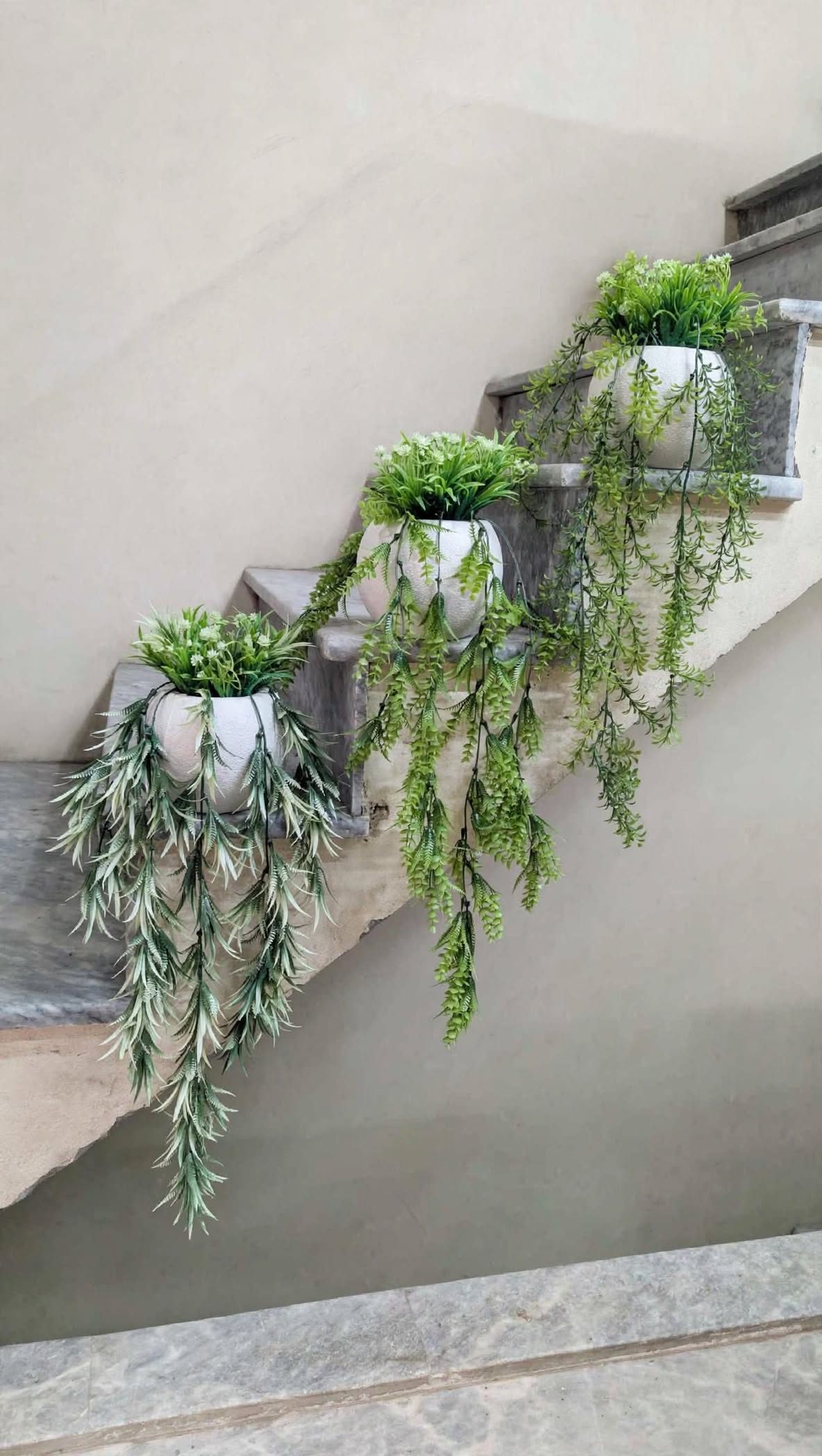 Three artificial hanging plant pot arrangements on marble stairs