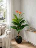 48-inch decorative floor plant with lush green leaves, orange flowers, and rounded black pot beside a sofa