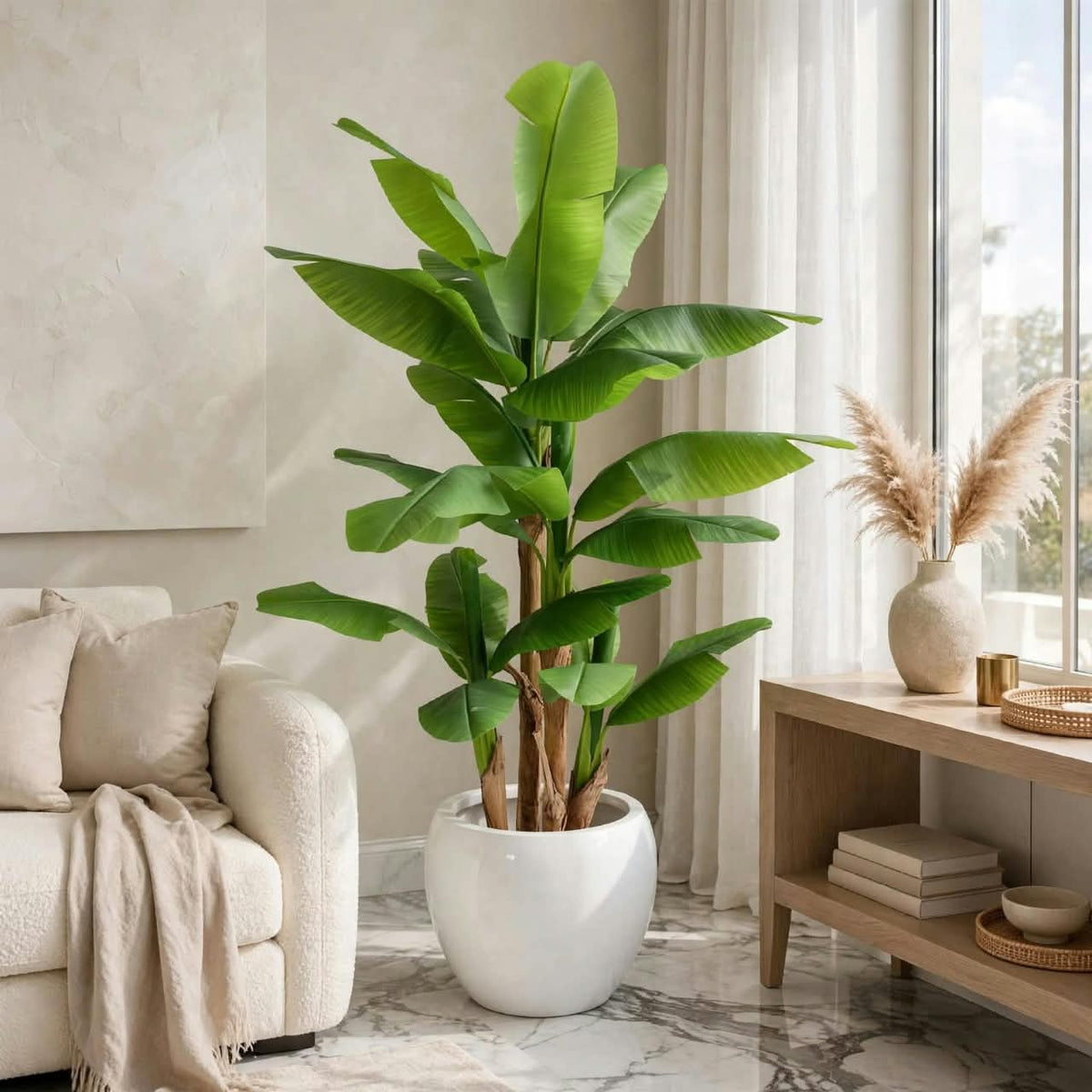 Large artificial banana leaf tree with twin trunks styled in a bright luxury living room with white pot