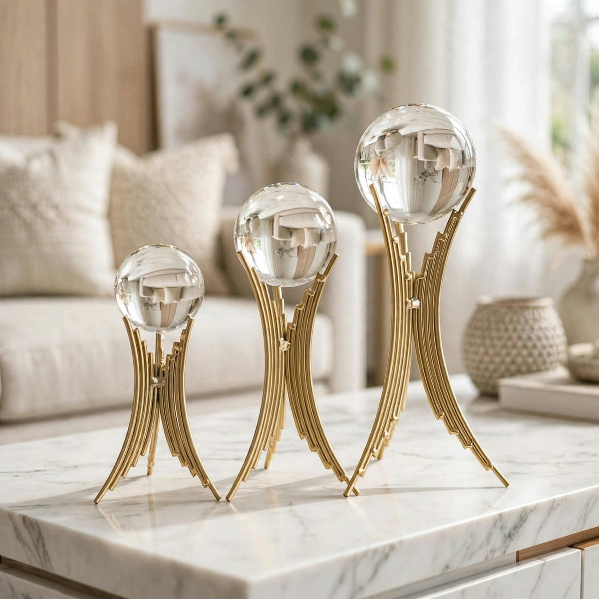 Set of 3 crystal ball sculptures on gold arch stands displayed on a marble coffee table in a luxury living room